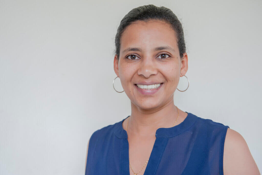 Adugna smiling. The young Ethiopian woman is wearing big silver loop earrings and a blue top