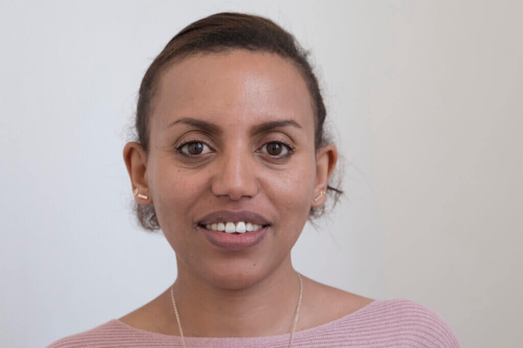 Alem, a young Ethiopian woman in a light pink top looks straight into the camera.