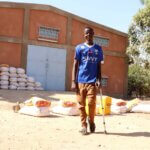 Disability-inclusive humanitarian action in practice: a young man with a crutch collects food aid at an IMPACT-BF site in Ouagadougou, Burkina Faso.