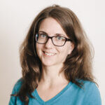 Portrait of Ursula Miller, Expert Partnerships. She has long brown hair and glasses, smiles at the camera and wears a turquoise jumper.