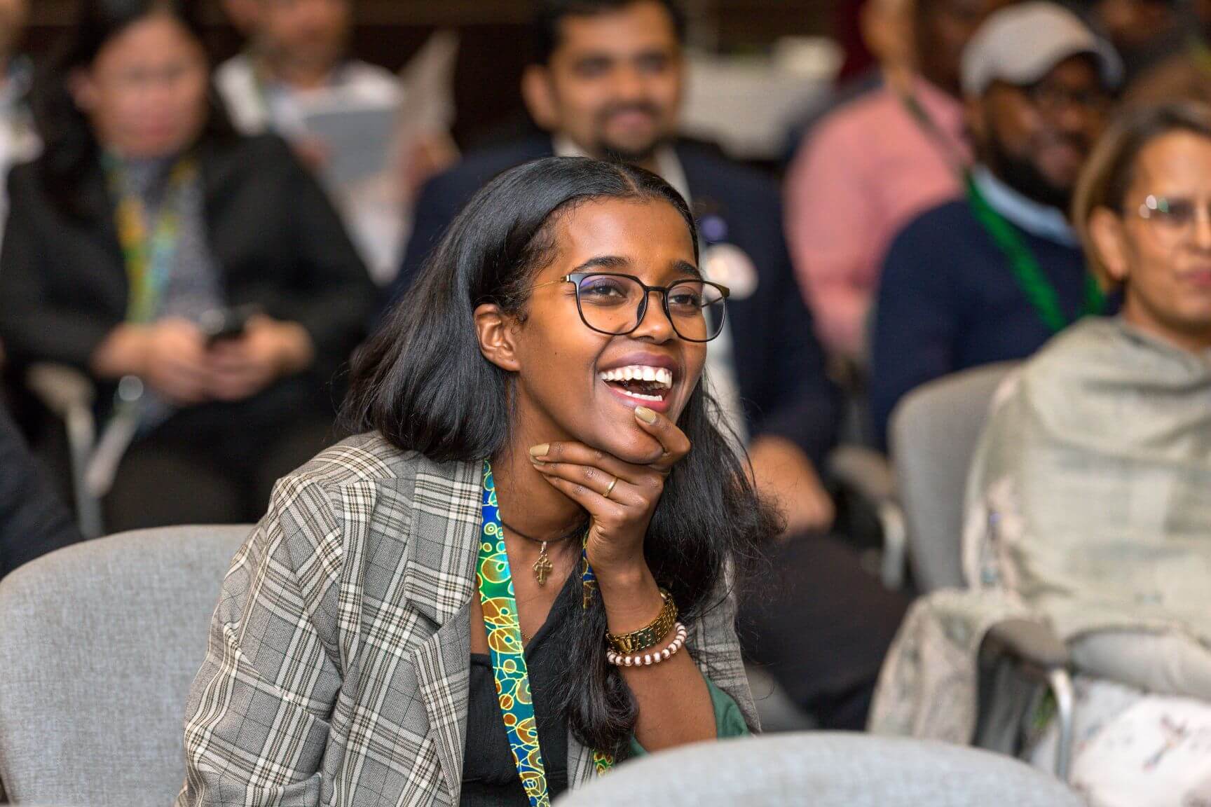 Biruktayit Kefyalew, Light for the World's Expert, Eye Health, laughs during a session at an international conference. She is wearing glasses and a grey blazer, with a colourful lanyard, and is seated among other delegates in the background.